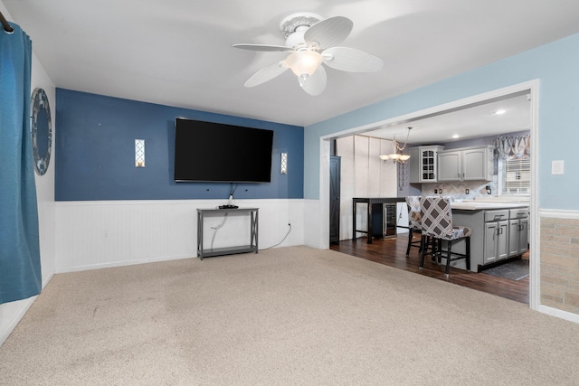 carpeted living room featuring ceiling fan with notable chandelier