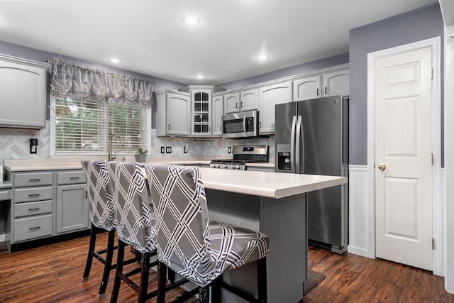 kitchen with appliances with stainless steel finishes, gray cabinets, a kitchen island, dark hardwood / wood-style floors, and a breakfast bar area