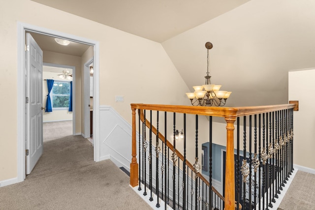 hallway with an inviting chandelier, vaulted ceiling, and light colored carpet