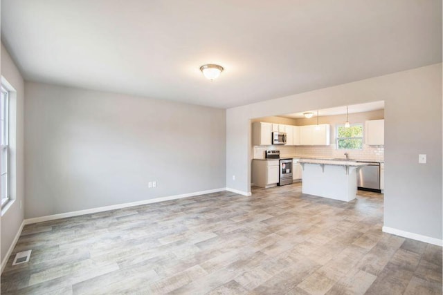 kitchen featuring tasteful backsplash, stainless steel appliances, a center island, white cabinetry, and hanging light fixtures