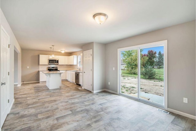 kitchen with light wood-type flooring, stainless steel appliances, pendant lighting, a center island, and white cabinetry