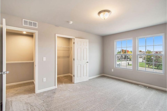 unfurnished bedroom with a spacious closet, a closet, and light colored carpet