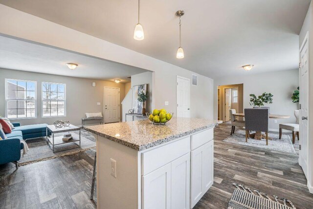 kitchen with a kitchen island, light stone counters, dark hardwood / wood-style floors, pendant lighting, and white cabinets