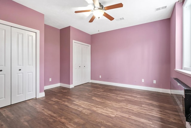 unfurnished bedroom featuring two closets, ceiling fan, and dark wood-type flooring