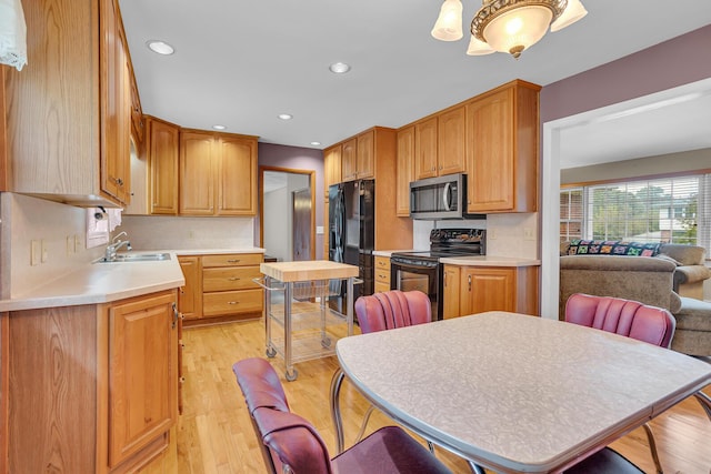 kitchen with backsplash, black appliances, sink, light wood-type flooring, and decorative light fixtures