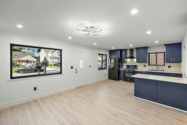 kitchen with blue cabinetry, sink, wall chimney exhaust hood, light hardwood / wood-style floors, and black appliances