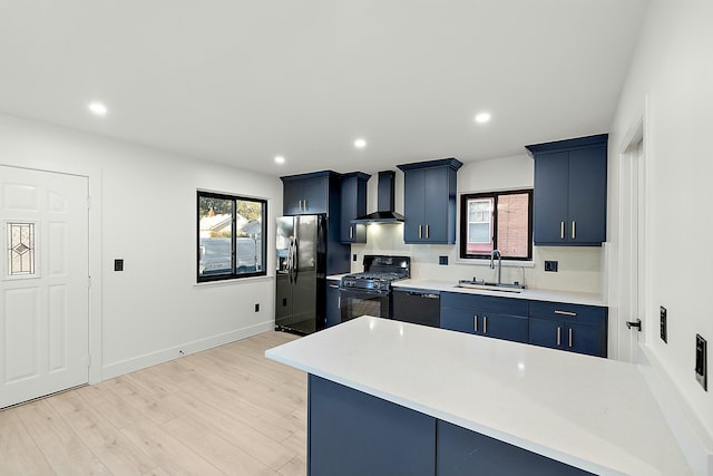 kitchen with blue cabinetry, sink, wall chimney exhaust hood, light hardwood / wood-style flooring, and black appliances