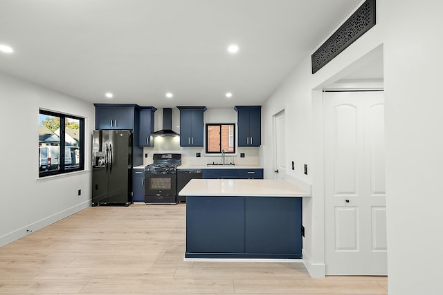 kitchen with kitchen peninsula, light wood-type flooring, wall chimney range hood, sink, and black appliances