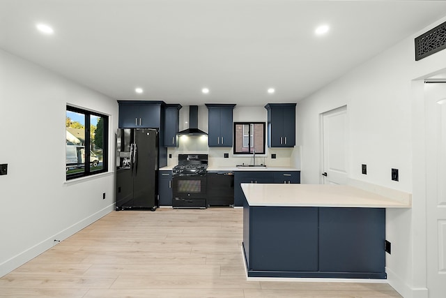 kitchen with kitchen peninsula, wall chimney exhaust hood, sink, black appliances, and light hardwood / wood-style flooring