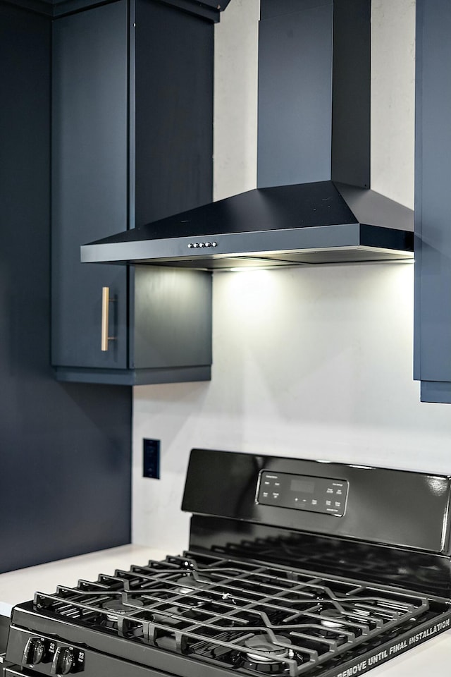 kitchen featuring gas stove, wall chimney range hood, and blue cabinets