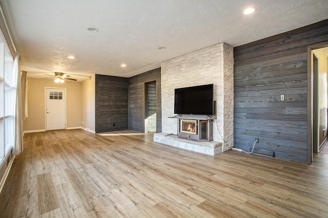 unfurnished living room featuring ceiling fan, light hardwood / wood-style floors, a textured ceiling, and wooden walls