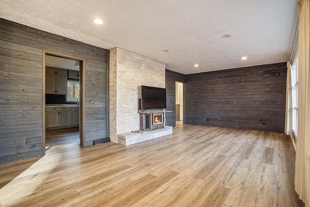 unfurnished living room featuring a wood stove, wooden walls, and light wood-type flooring