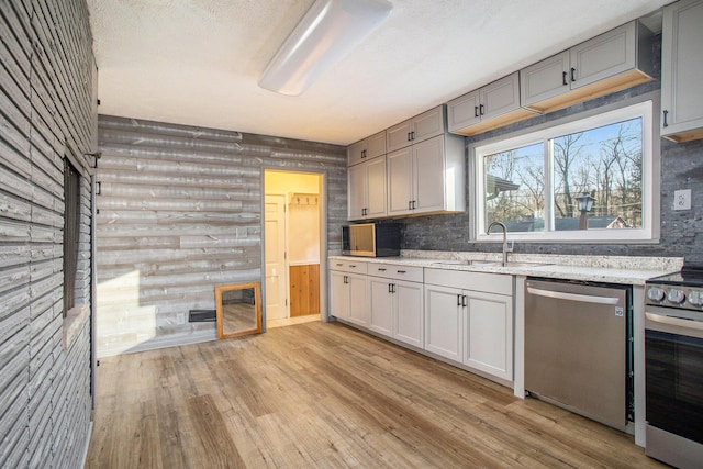 kitchen featuring rustic walls, gray cabinetry, sink, light hardwood / wood-style flooring, and appliances with stainless steel finishes