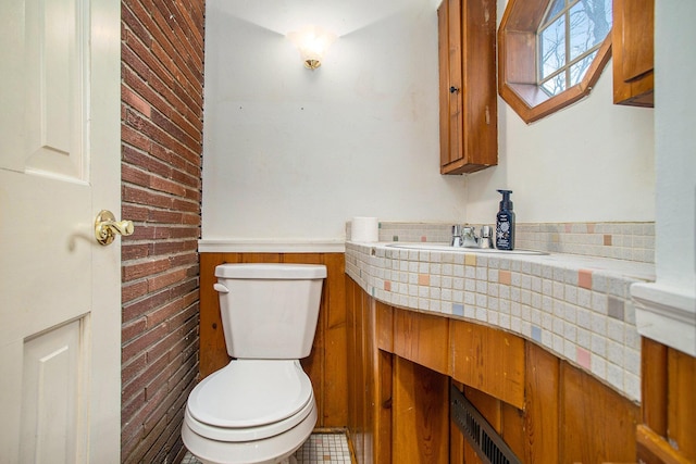 bathroom featuring vanity, brick wall, and toilet