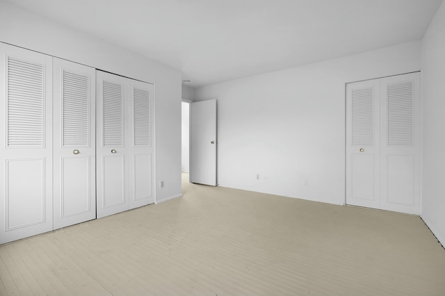 unfurnished bedroom with light wood-type flooring and two closets