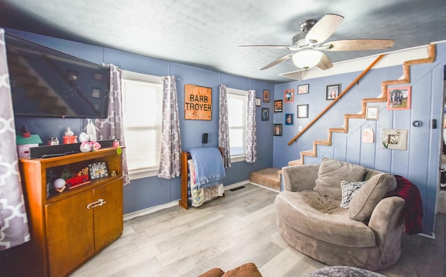 living room with ceiling fan, a textured ceiling, and light wood-type flooring