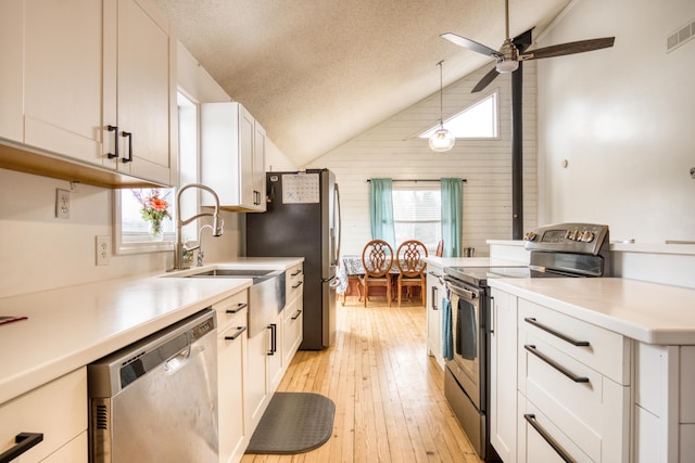 kitchen featuring a textured ceiling, decorative light fixtures, lofted ceiling, white cabinets, and appliances with stainless steel finishes