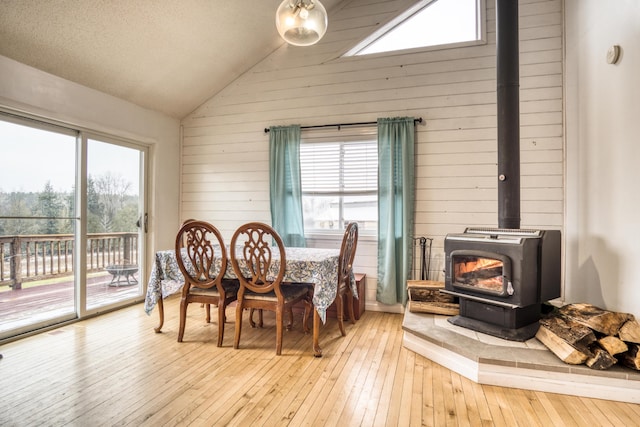 dining room with light hardwood / wood-style flooring, a wood stove, lofted ceiling, and wood walls