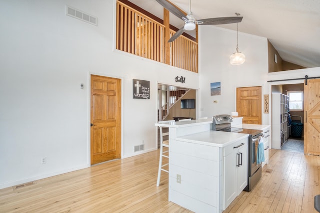 kitchen featuring a barn door, white cabinets, stainless steel range with electric stovetop, and high vaulted ceiling