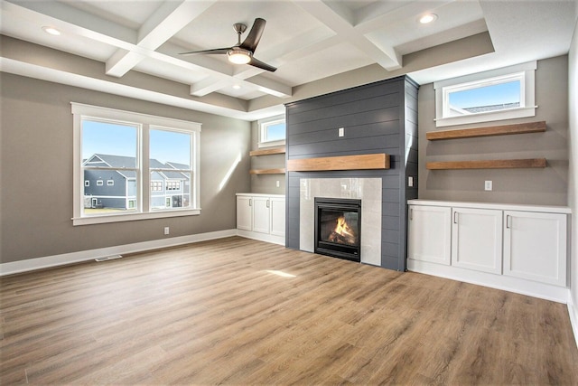 unfurnished living room featuring light wood-type flooring, a wealth of natural light, coffered ceiling, a tile fireplace, and beamed ceiling