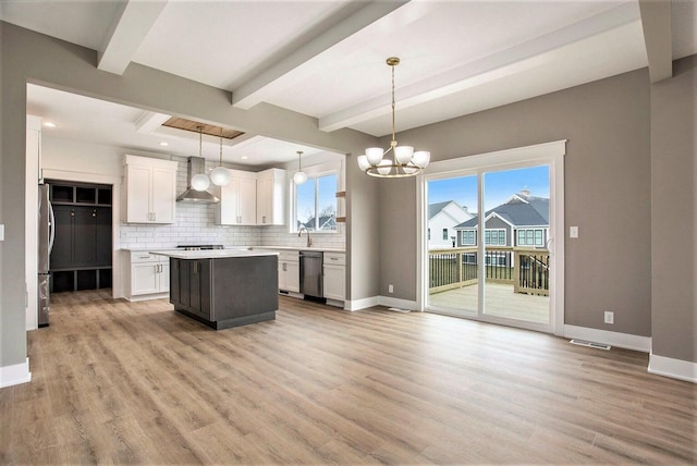 kitchen with a center island, wall chimney exhaust hood, stainless steel appliances, decorative light fixtures, and white cabinets