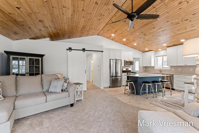 living room with ceiling fan, sink, a barn door, wooden ceiling, and lofted ceiling