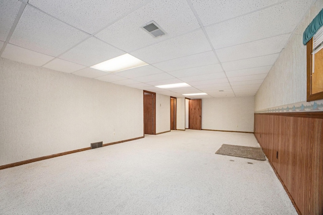 basement featuring a paneled ceiling, wood walls, and light colored carpet