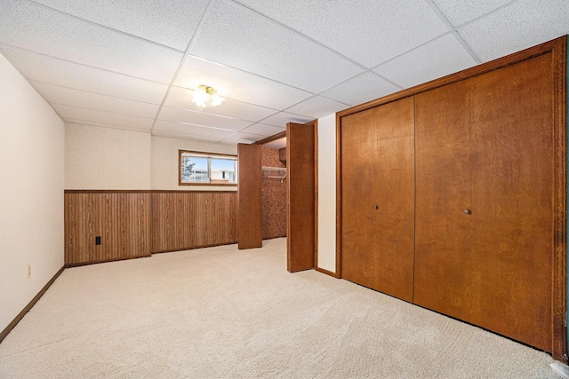 basement with light colored carpet, a drop ceiling, and wood walls