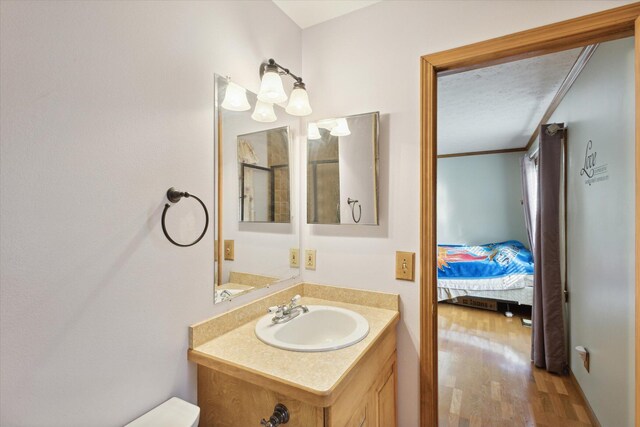 bathroom with a textured ceiling, vanity, crown molding, hardwood / wood-style flooring, and toilet