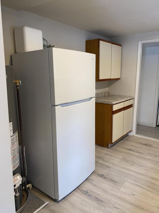 kitchen with white fridge, light wood-type flooring, white cabinetry, and water heater