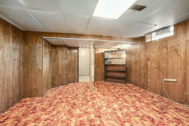 interior space with a paneled ceiling, wood walls, and carpet floors