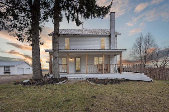 back house at dusk featuring a porch and a lawn