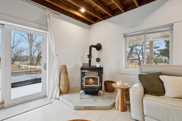 interior space featuring beam ceiling, a wood stove, plenty of natural light, and wooden ceiling