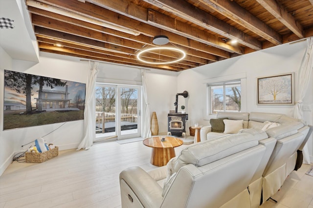 living room featuring beamed ceiling, plenty of natural light, a wood stove, and wooden ceiling