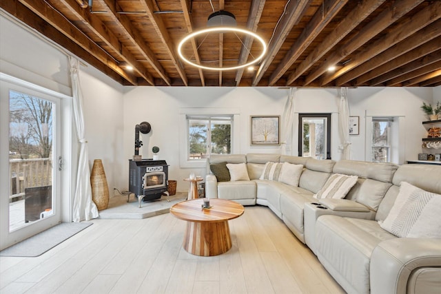 living room with beamed ceiling, light hardwood / wood-style flooring, a wood stove, and wooden ceiling