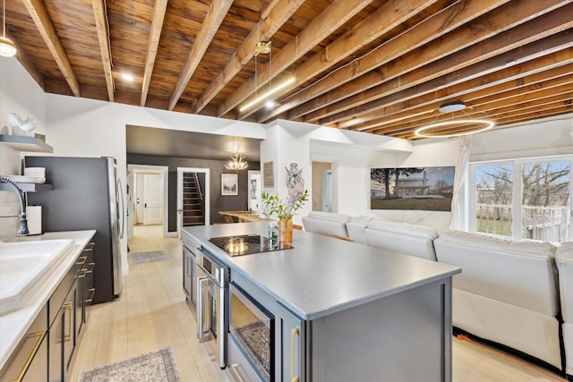 kitchen featuring wood ceiling, black electric cooktop, sink, beamed ceiling, and a kitchen island