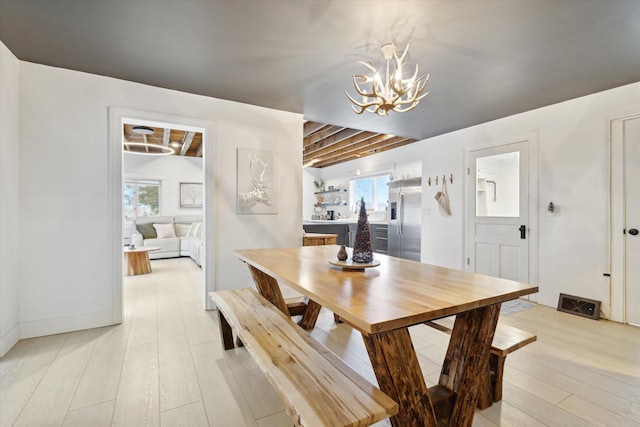 dining space featuring beamed ceiling, light hardwood / wood-style floors, and a notable chandelier