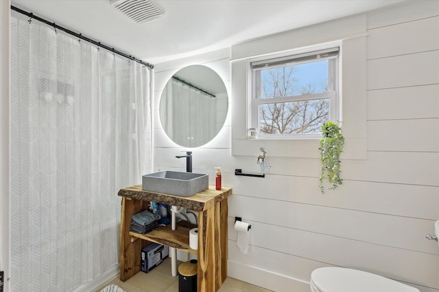 bathroom featuring a shower with shower curtain, toilet, wooden walls, and sink