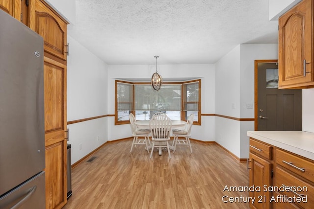 dining space with a textured ceiling, light hardwood / wood-style flooring, and a notable chandelier