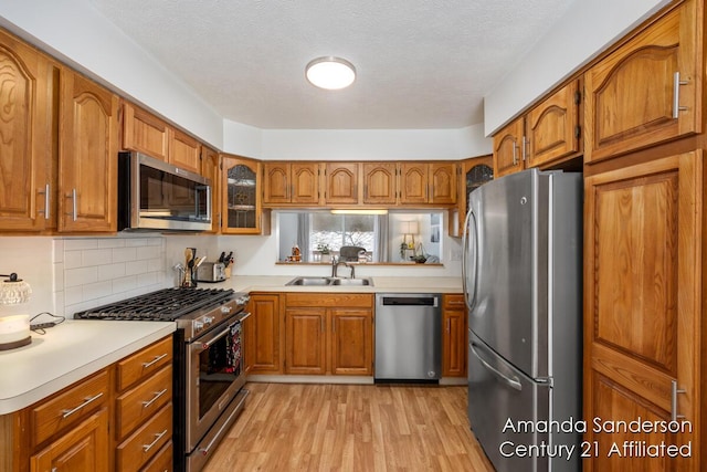 kitchen with decorative backsplash, a textured ceiling, stainless steel appliances, sink, and light hardwood / wood-style flooring