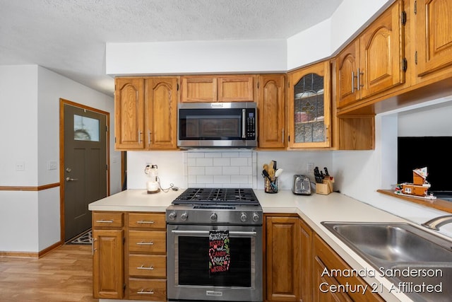 kitchen featuring sink, a textured ceiling, decorative backsplash, appliances with stainless steel finishes, and light wood-type flooring