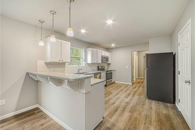 kitchen featuring hanging light fixtures, white cabinetry, a kitchen bar, kitchen peninsula, and stainless steel appliances