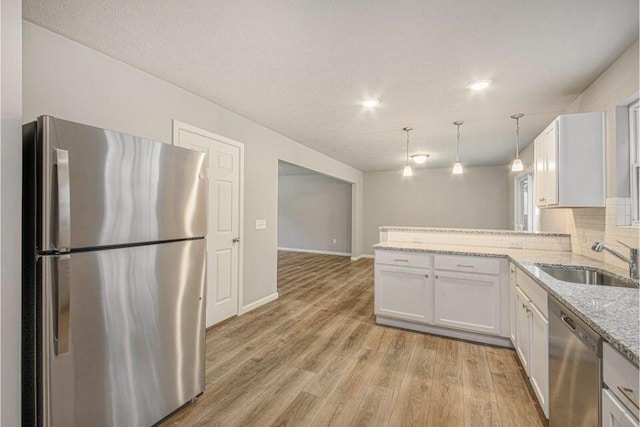 kitchen with white cabinetry, sink, kitchen peninsula, pendant lighting, and appliances with stainless steel finishes