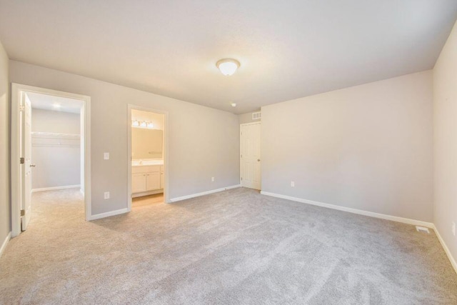 unfurnished bedroom featuring a walk in closet, light carpet, connected bathroom, and a closet