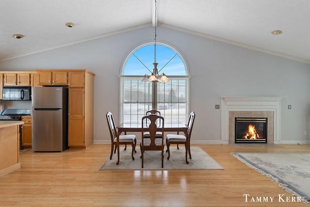 dining space with lofted ceiling, a tile fireplace, crown molding, light hardwood / wood-style floors, and a chandelier