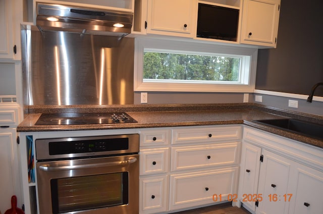 kitchen featuring stainless steel oven, sink, black electric cooktop, and white cabinetry