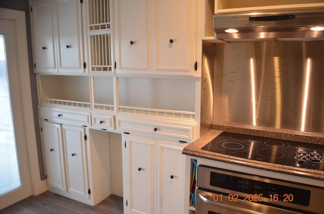 kitchen featuring black electric stovetop, hardwood / wood-style floors, stainless steel oven, and white cabinets