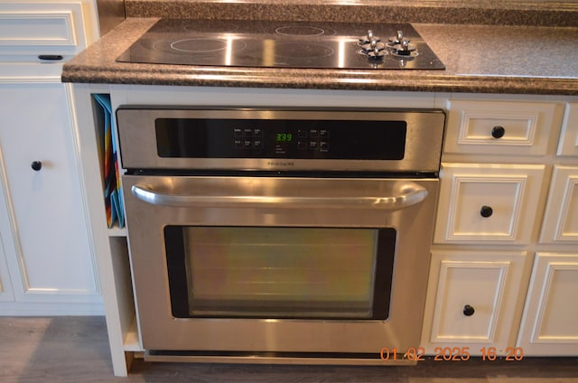 interior details with black electric cooktop, stainless steel oven, and white cabinets