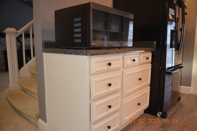 kitchen featuring white cabinetry, black fridge, hardwood / wood-style floors, and dark stone countertops