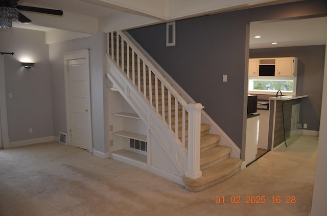 stairway with carpet floors, sink, and ceiling fan